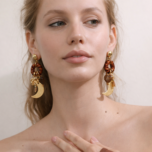 Woman wearing gold and brown earrings with a neutral background