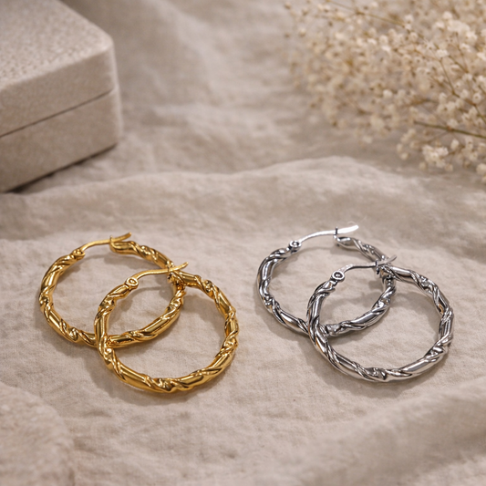 Gold and silver hoop earrings on a textured surface with a neutral background