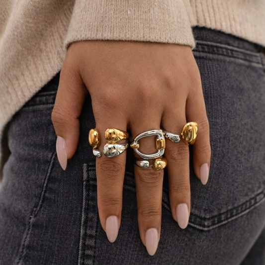 Hand wearing multiple statement rings with gold and silver designs on a dark background