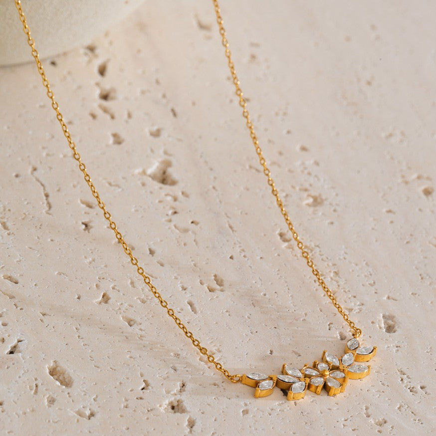 Gold necklace with floral pendant on a beige stone surface