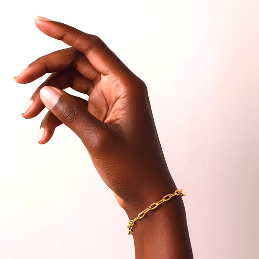 Hand wearing a gold chain bracelet on a light background