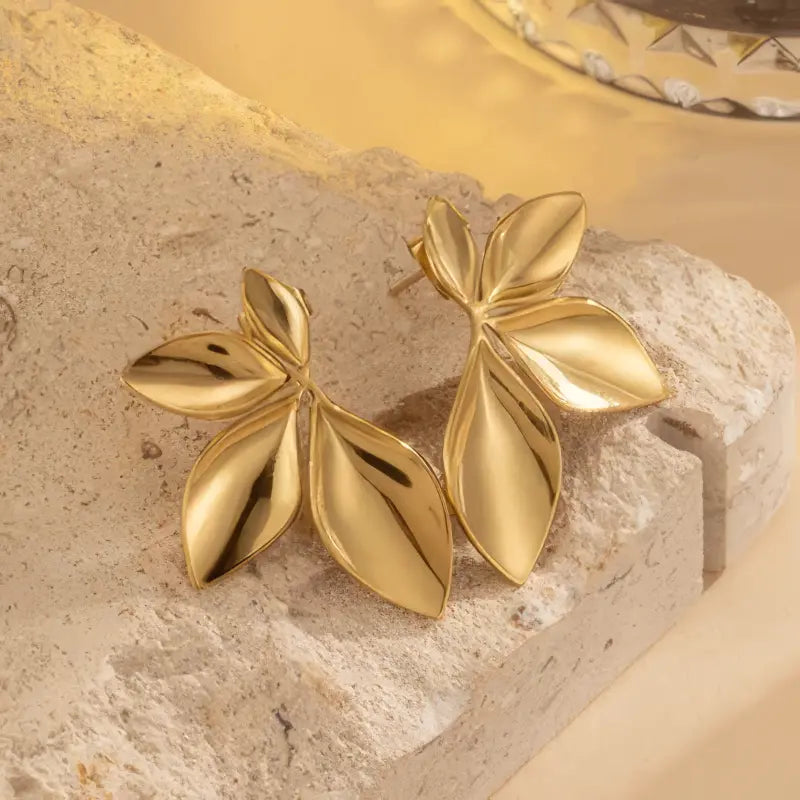 Gold leaf-shaped earrings on a textured stone surface