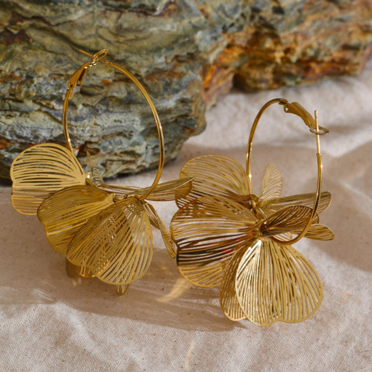Gold statement earrings on a textured surface with a stone background
