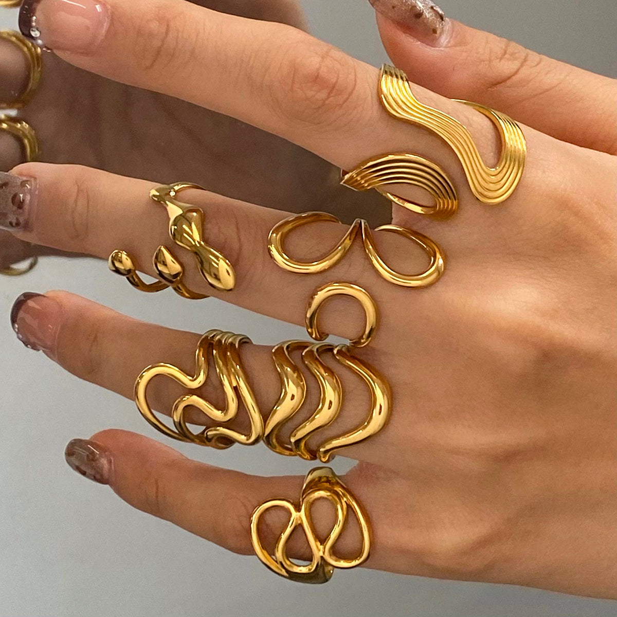 Gold ring collection on a hand against a neutral background