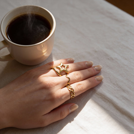 Hand with gold rings on a table next to a cup of coffee