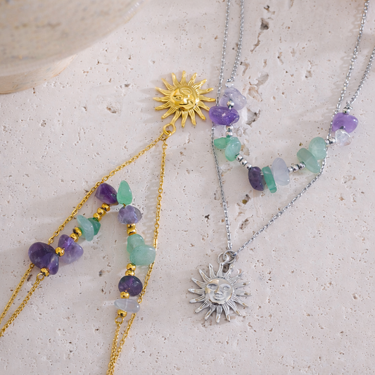 Two sun-shaped necklaces with gemstones on a textured surface