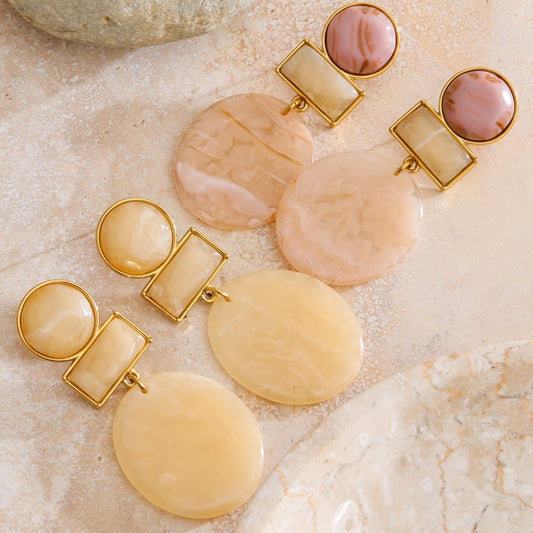 Pair of earrings with gold and stone-like components on a textured beige surface