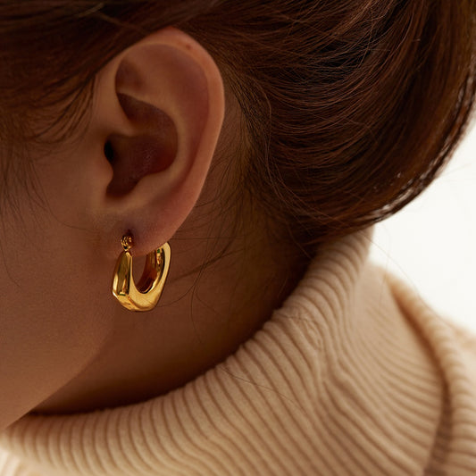 Close-up of an ear wearing a gold hoop earring with a blurred background