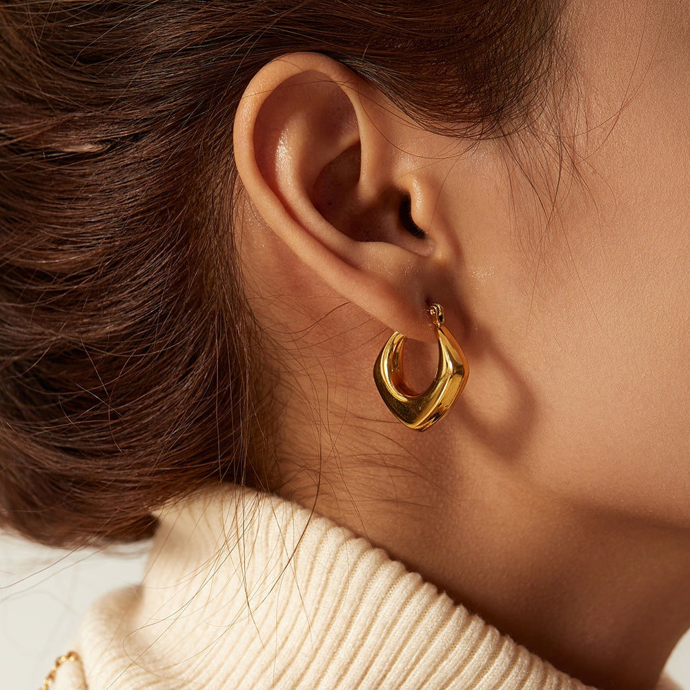 Close-up of a person wearing a gold hoop earring with a neutral background