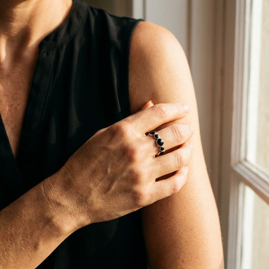 Person wearing a black sleeveless top with a tarnish-free ring on their hand, sitting by a window.