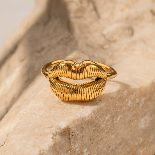 Gold lip-shaped ring on a textured beige surface