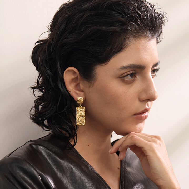 Woman wearing long gold earrings with a neutral background