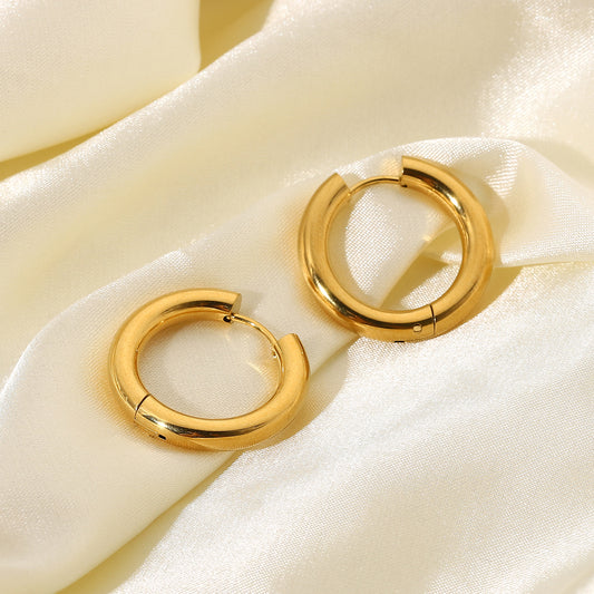 Minimalist gold hoop earrings on a soft beige fabric background