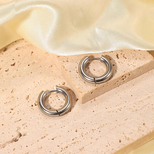 Pair of simple silver hoop earrings on a beige stone surface with a light fabric background
