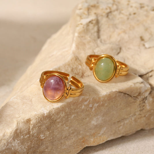 Two gold rings with gemstones on a stone surface