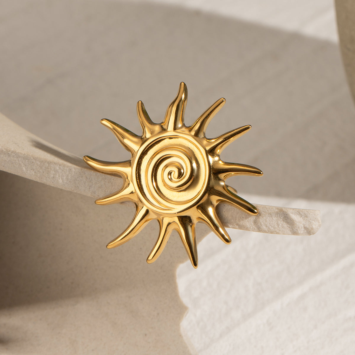 Gold sun-shaped statement ring on a beige surface