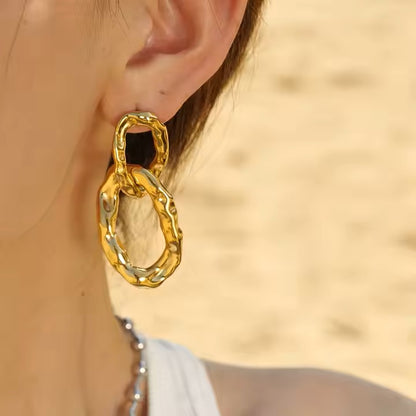 Gold chain-style earring worn by a person with a blurred background
