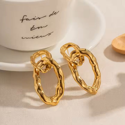 Gold hoop earrings on a beige surface with a white dish in the background