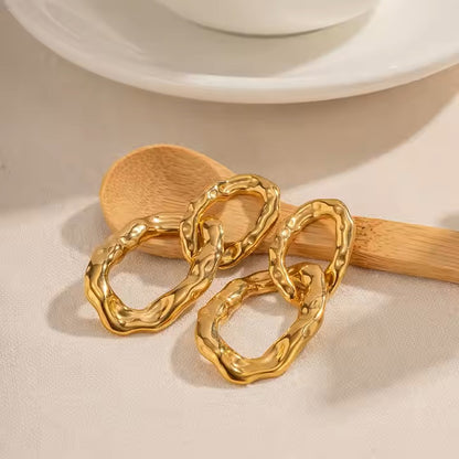 Gold statement earrings on a wooden spoon with a beige background