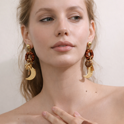 Woman wearing gold and brown earrings with a neutral background
