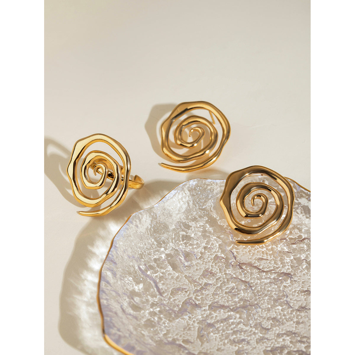 Gold spiral earrings and ring on a textured stone surface
