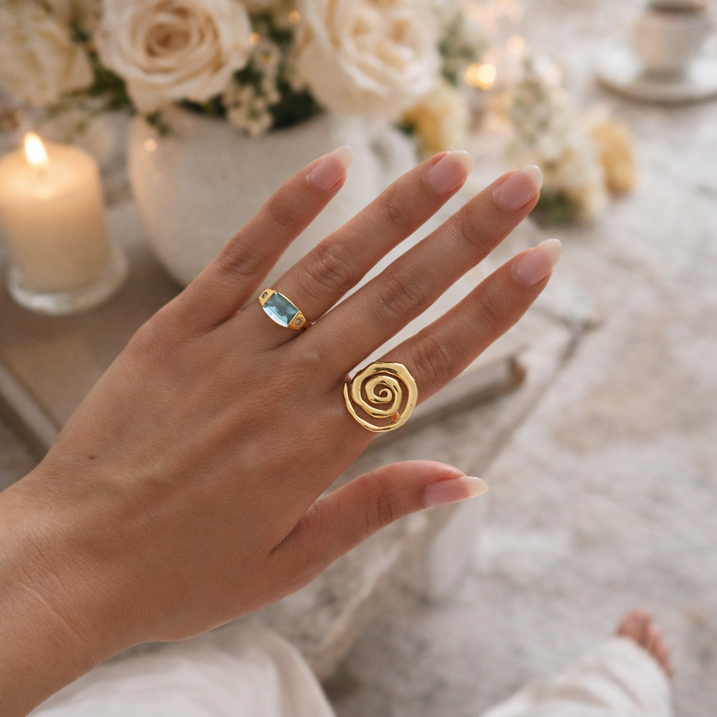 Hand wearing two gold rings with a blurred background of flowers and candles
