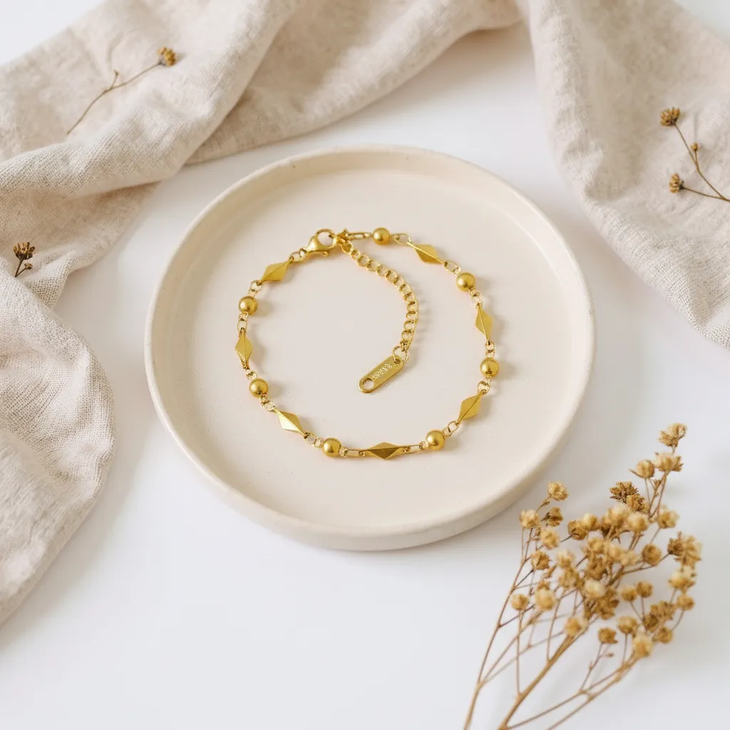 Gold bracelet on a white plate with beige fabric and dried flowers in the background