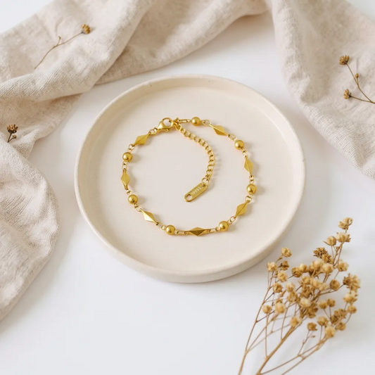 Gold bracelet on a white plate with beige fabric and dried flowers in the background