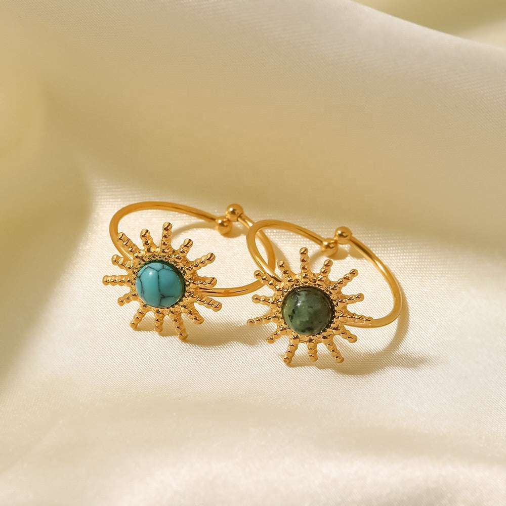 Gold rings with turquoise and green gemstones on a beige fabric background