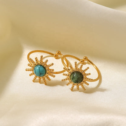 Gold rings with turquoise and green gemstones on a beige fabric background