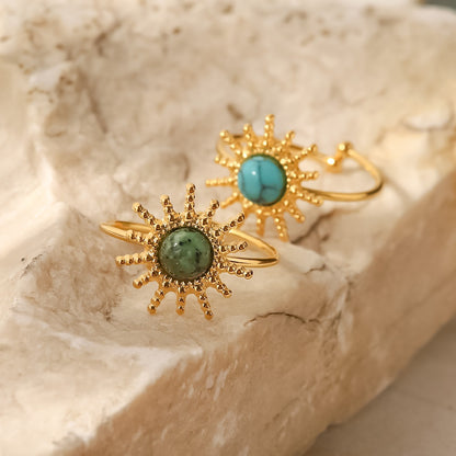 Two gold rings with turquoise stones on a beige stone surface