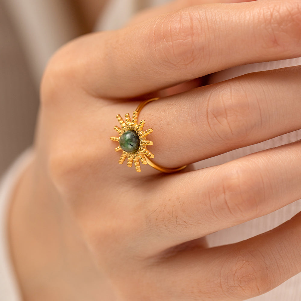 Gold ring with a green gemstone on a hand against a neutral background