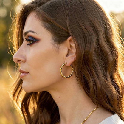 Woman wearing gold hoop earrings with a blurred natural background