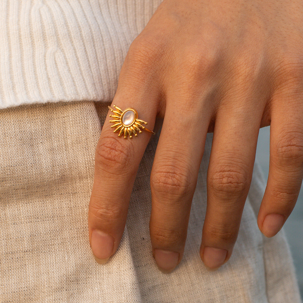 Hand wearing a gold ring with a stone, set against a neutral background