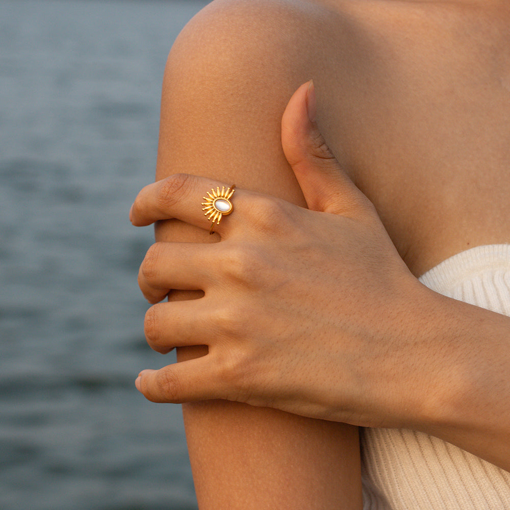 Close-up of a person's hand with a gold ring featuring a sun design, against a blurred natural background.