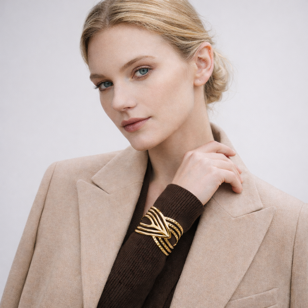 Woman wearing a beige blazer with a gold statement bracelet on a plain background