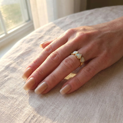 Hand wearing a gold ring with pearls on a textured surface