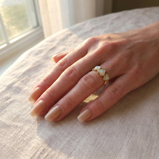 Hand wearing a gold ring with pearls on a textured surface