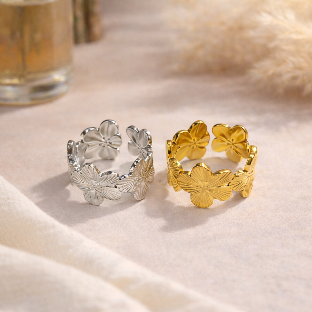 Two floral-patterned rings, one gold and one silver, on a soft fabric background.