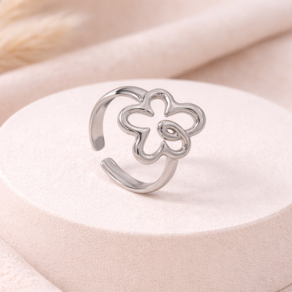 Silver flower-shaped ring on a white cushion with a beige background