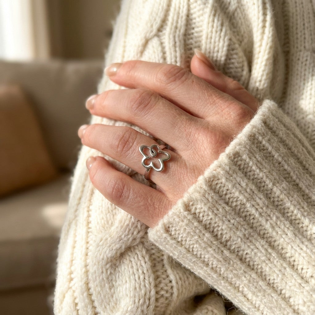 Hand wearing a silver ring with a flower design, held against a beige sweater.