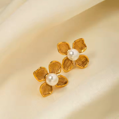 Gold flower-shaped earrings with pearl centers on a beige background
