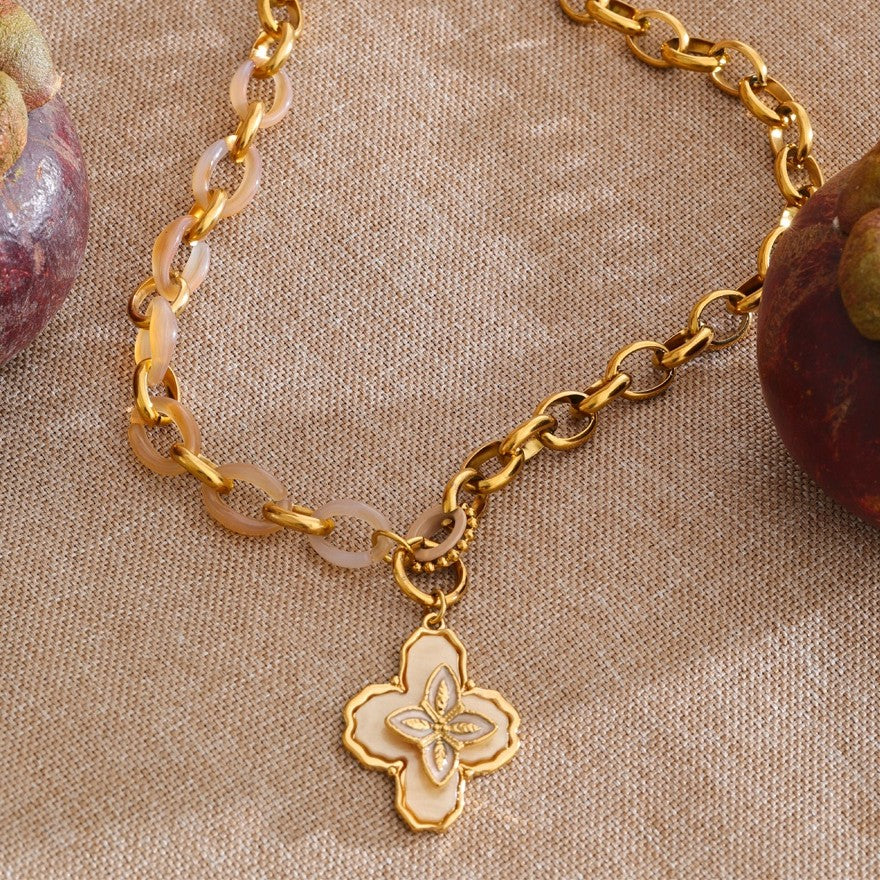 Gold chain necklace with a floral charm on a beige fabric background