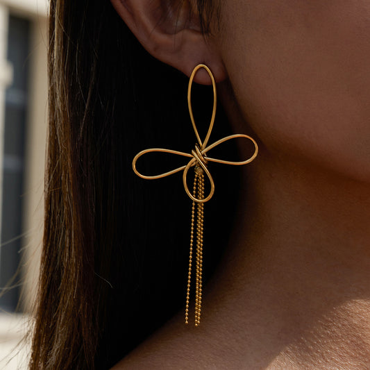 Gold statement bow-shaped earring with dangling beads worn by a person.