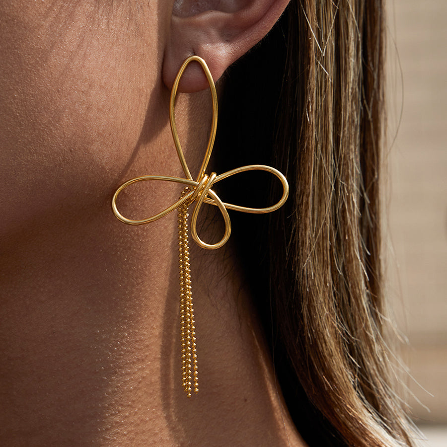 Gold bow-shaped earring with dangling beads worn by a person.
