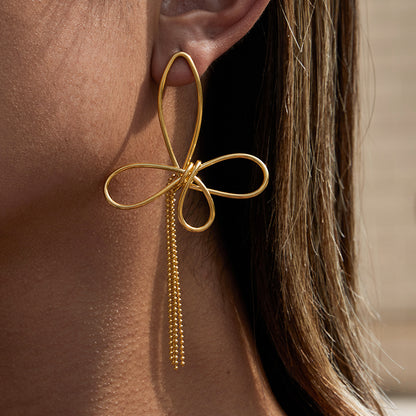 Gold bow-shaped earring with dangling beads worn by a person.