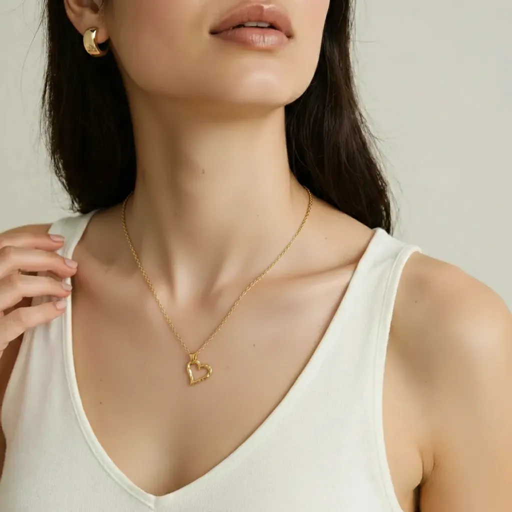 Woman wearing a gold heart-shaped necklace with a plain background
