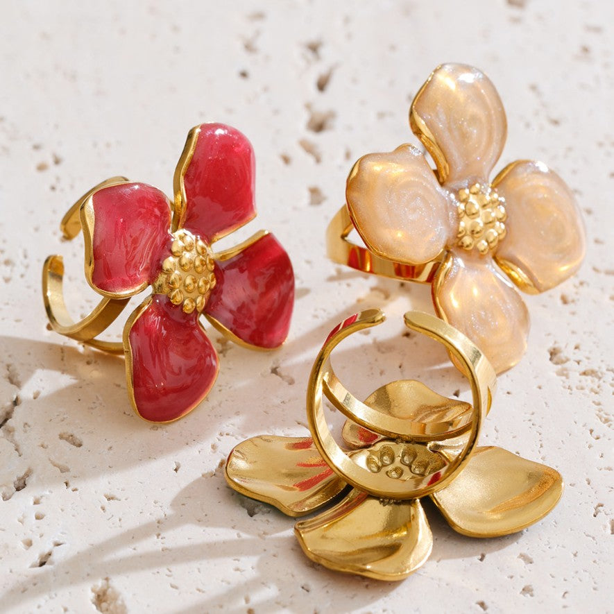 Three floral-shaped rings in red, gold, and beige on a textured surface.