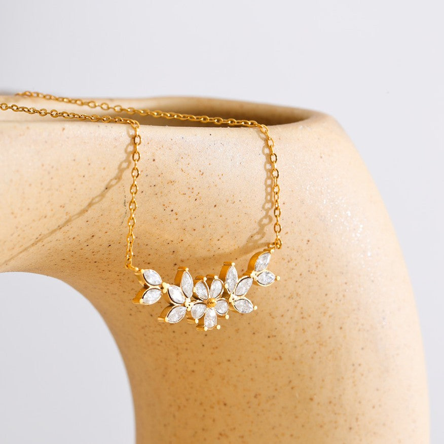 Gold necklace with a floral pendant on a beige mannequin against a light gray background