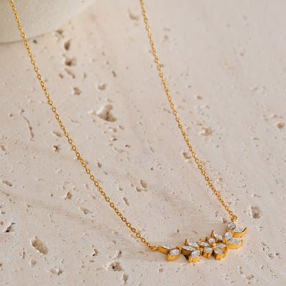 Gold necklace with floral pendant on a beige stone surface